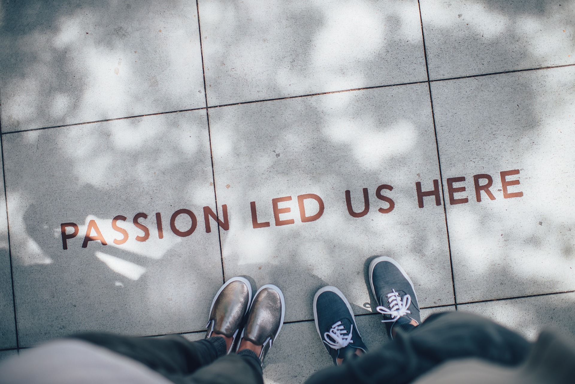 Top-view of a person's feet on a street walkway with the text 'Passion Led Us Here'