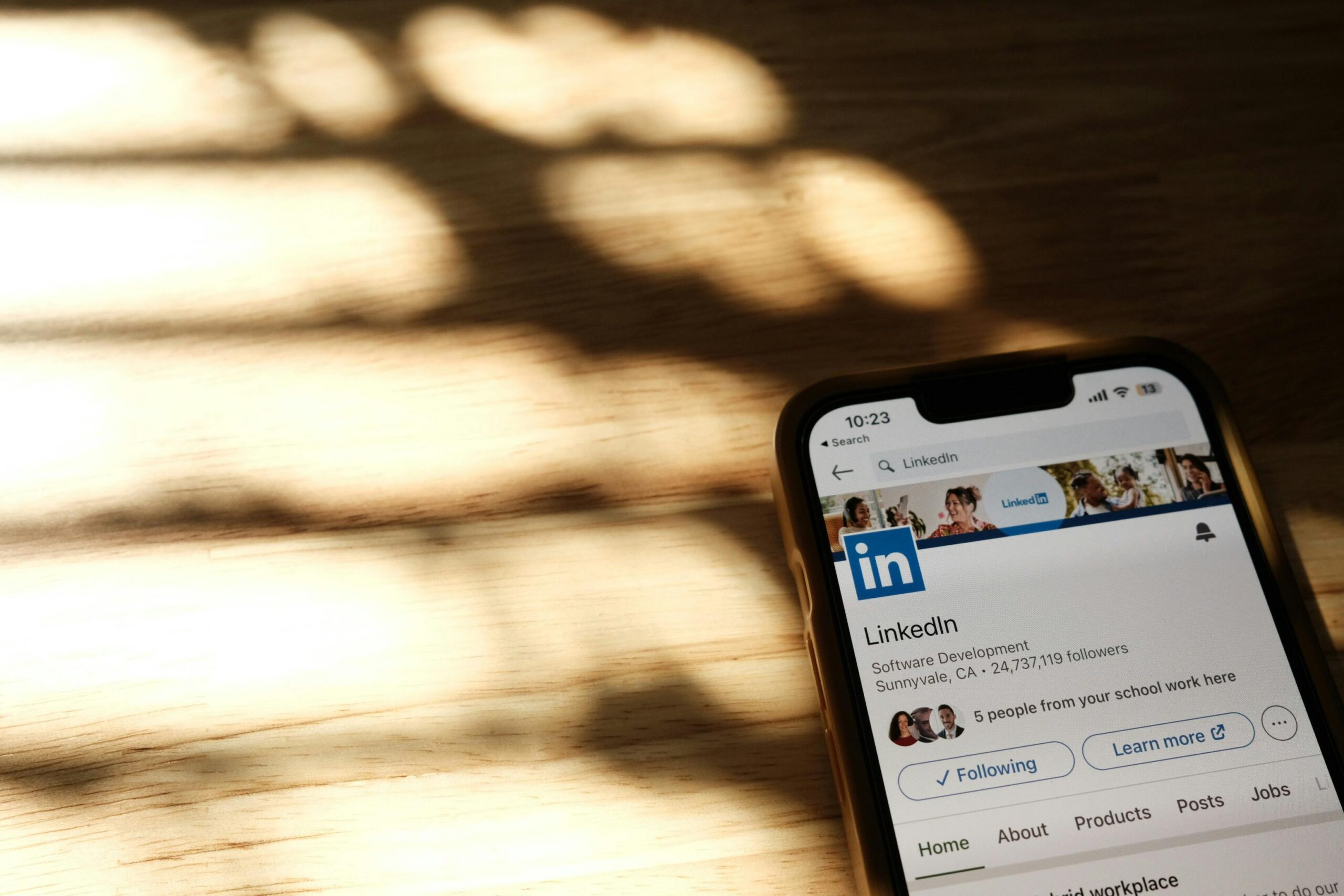Smartphone displaying the LinkedIn app profile page on a wooden table with soft sunlight and shadows.