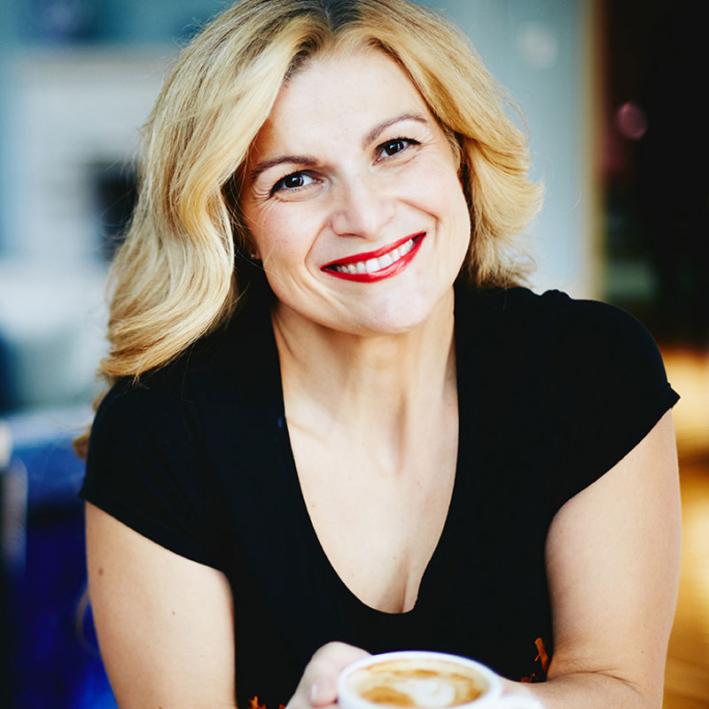 Despina Karatzias a smiling woman with blonde hair holding a cup of coffee, exuding warmth and positivity