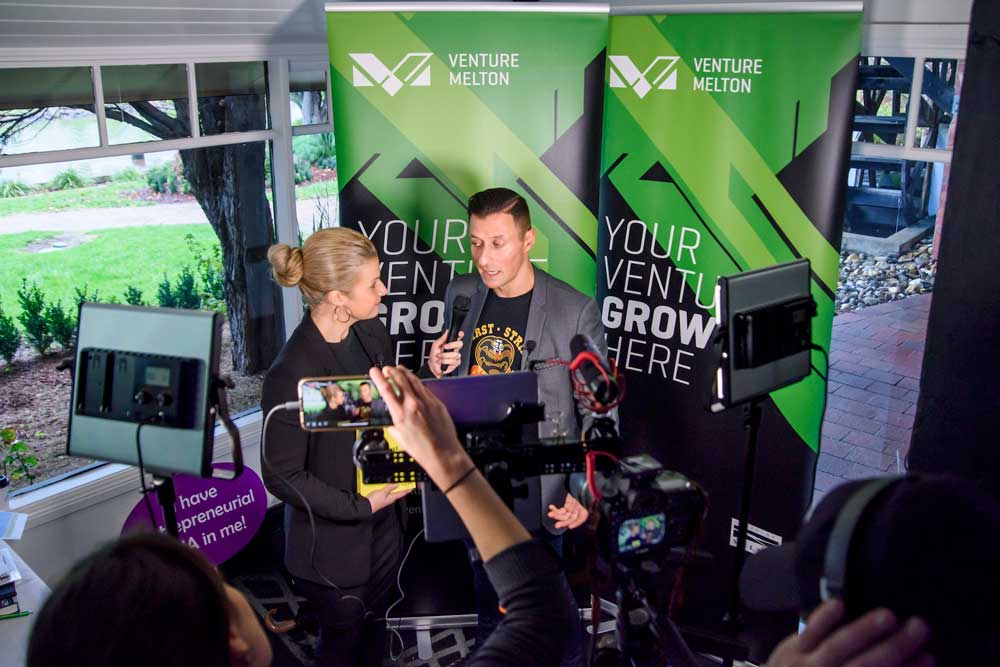Despina Karatzias interviewing an entrepreneur at a Venture Melton event, surrounded by professional video and lighting equipment.