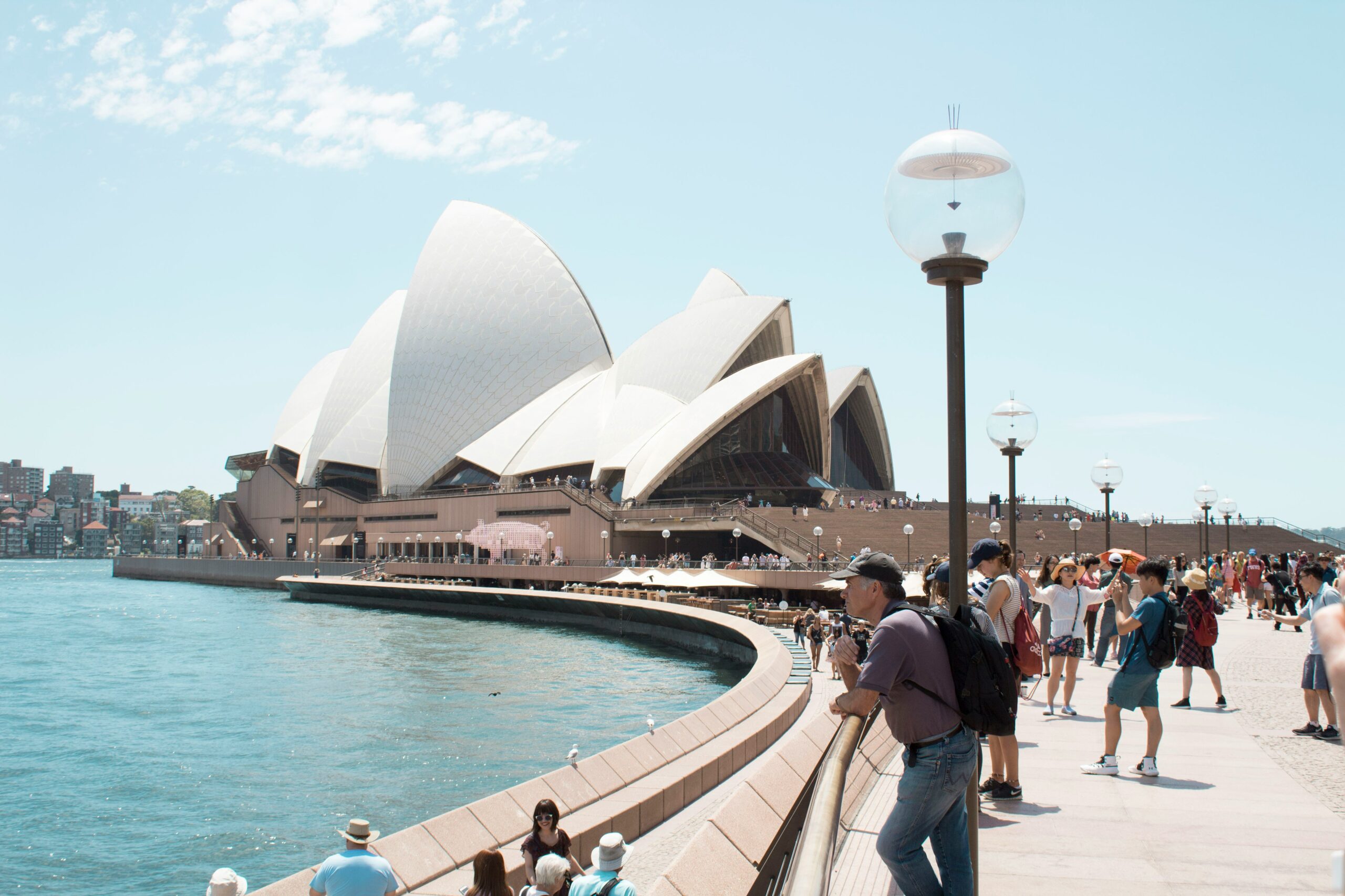 Sydney Opera House and its surrounding promenade bustling with visitors on a sunny day.