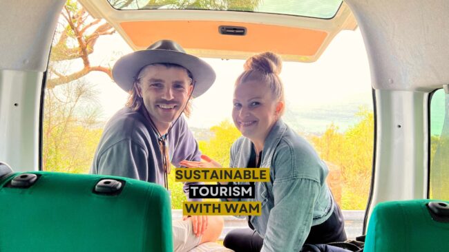 Sustainable Tourism with WAM Man in a hat and woman smiling inside a van with text overlay: Sustainable Tourism with WAM, overlooking a scenic landscape.