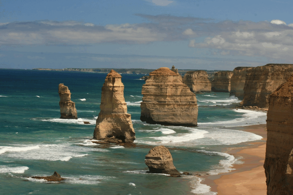 The Twelve Apostles limestone stacks rising from the Southern Ocean along Victoria’s Great Ocean Road, with waves breaking against the cliffs and shoreline.