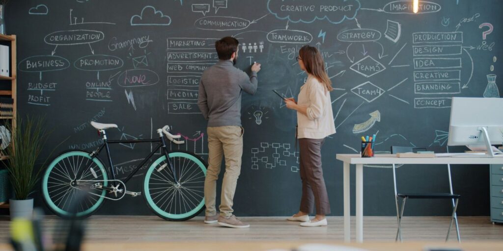 Two business professionals mapping ideas and strategy on a chalkboard in a modern workspace.