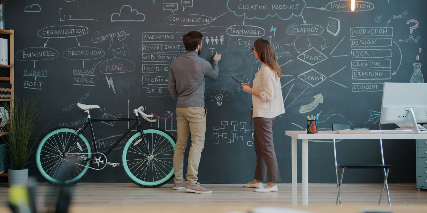 Two business professionals mapping ideas and strategy on a chalkboard in a modern workspace.