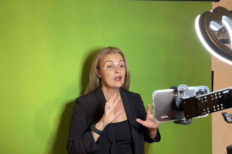 Despina Karatzias speaking to a phone on a tripod with a ring light and green screen while batch recording videos for a 30-day marketing challenge